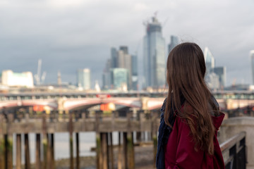 Fototapeta na wymiar London tourist enjoying the view of City of London skyscrapers. Young traveler woman looking at the City of London from the south bank of the River Thames during the low tide.