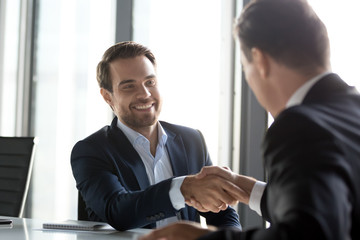 Happy businessmen in suits shaking hands after successful negotiations at meeting, male partners...