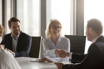 Happy mature businesswoman handshaking new male partner, ceo and smiling middle aged lady shaking...