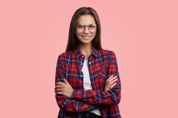 Glad female model crosses hands over chest, isolated over pink background. People, youth, emotions concept