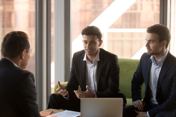Arabic businessman talking at group meeting convincing client promising benefits, confident arab adviser speaking making business offer negotiating with caucasian partners presenting idea to investor
