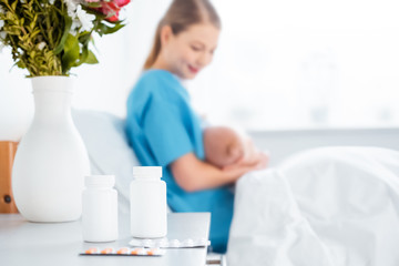 close-up view of pills, flowers in vase and young mother breastfeeding newborn baby in hospital room