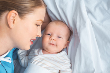 happy young mother looking at adorable newborn baby lying on bed