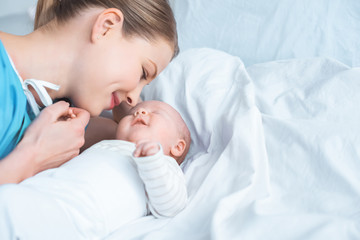 smiling young mother holding hand of adorable newborn baby lying on bed