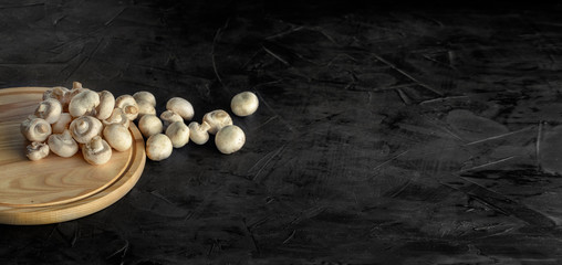 Fresh champignon mushrooms on a dark background. Top view, space for text