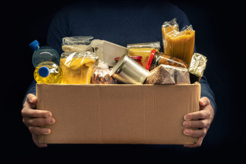 A man holding a donation box of different products on dark background - Powered by Adobe