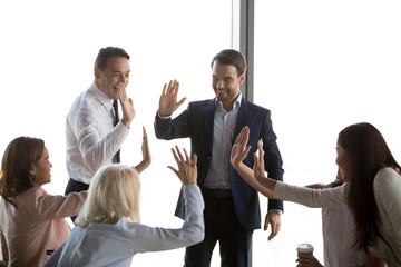 Excited diverse employees motivated happy executive office workers giving high five celebrating...