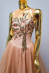 Obraz premium Long, light coffee designer, evening, women's dress handmade on gold, glossy mannequin. With white, gold, ornament in the form of a tree with leaves and red fruits from beads. Оn grаy background