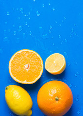 Fototapeta na wymiar Variety of ripe organic citrus fruits halved whole oranges sliced lemons on blue background with water drops. Summer refreshment drinks beverages juice cocktail ingredients. Vitamins healthy diet