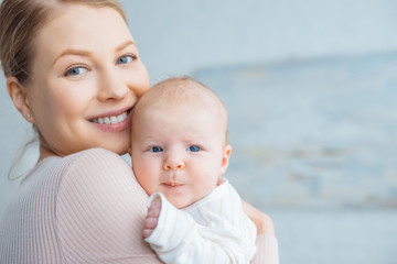 happy young mother carrying adorable baby and smiling at camera