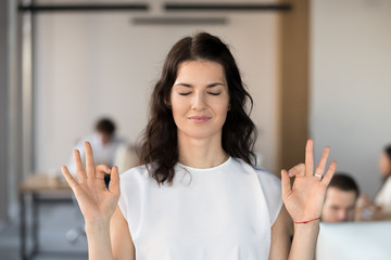 Young business woman employee meditating in office with eyes closed for no stress free relief, hoping for success, doing yoga exercise for relaxation or concentration at work, autosuggestion concept