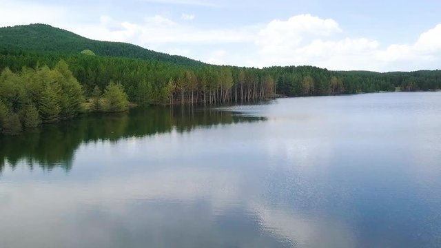 Aerial, drone shot, over a reflecting lake, towards forest and mountains, on a half cloudy, summer day, in Afyon, Afyonkarahisar region, Turkey