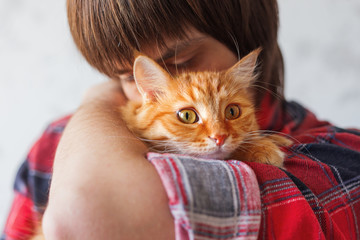 Man in tartan shirt holding cute ginger cat. Pet adoption, stray cat now has home. Fluffy pet looks puzzled.