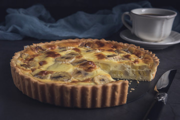 Sliced banana custard tart with cup of coffee. Horizontal