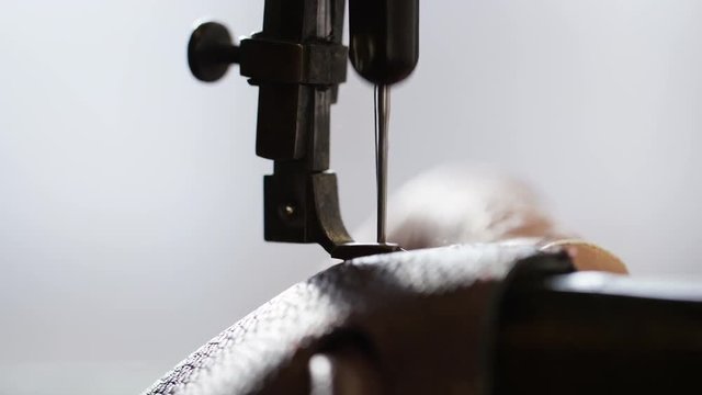 Needle of a traditional sewing machine stitching a leather handbag, in slow motion