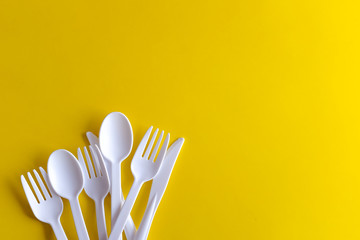Minimalistic white reusable plastic spoon fork knife cutlery isolated on yellow background laying on the table with copy space. Top view flat lay perspective. Plastic concern.