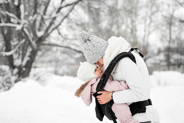 Little baby girl and her mother walking outside in winter Mother is holding her baby babywearing in...