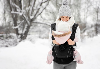 Little baby girl and her mother walking outside in winter Mother is holding her baby babywearing in...