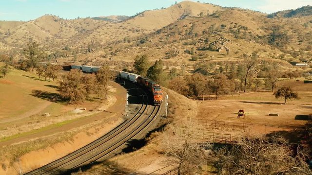The aerial camera flies in low head to head along the side of the locomotives. Then the camera does a 180 degree turn and begins to follow the train back into the eastern end of the rail loop tunnel.