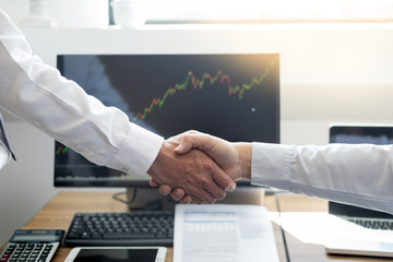 shaking Hand between businessman of cooperation over Stock market chart, business trading concept.