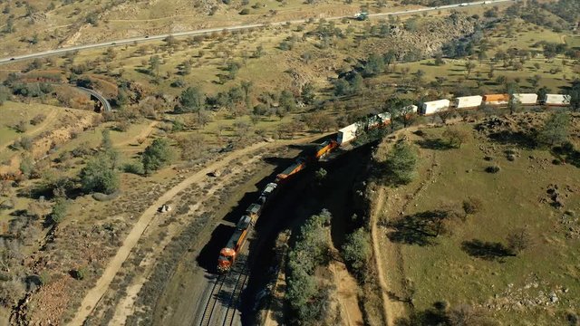 The aerial camera shoots 250 feet overhead of FOUR powerful diesel locomotives pulling a very long freight train coming around Cross Hill at the Tehachapi Railroad Loop.