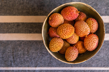 Litchi in a wooden bowl on a textile cowered table. Top view.