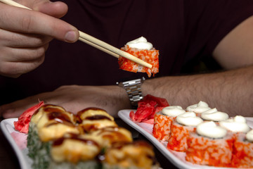closeup man eating delicious sushi with chopsticks with food in the background