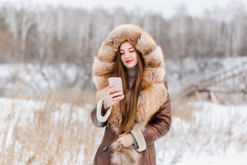 A beautiful girl in fur holds a phone in her hands and makes a selfie, a beautiful smile with white...