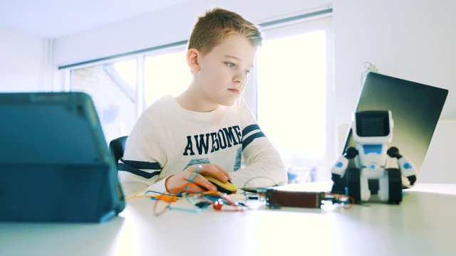 Boy works with electronics connected to laptop and looks at the screen