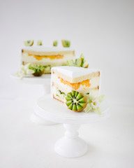 sponge cake with tropical fruit and vanilla cream on a white background on a white wooden stand