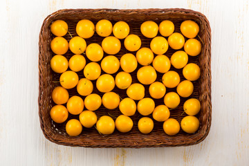Yellow cherry plums in basket - on white wooden surface