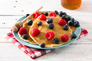 Pancakes with raspberries, blueberries and honey on white wooden table