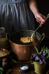Big vintage copper pan with soup and ladle in female hand.