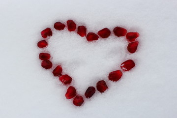 Valentine's heart shape made by pomegranate seeds on white snow. Valentine's Day concept. Selective focus