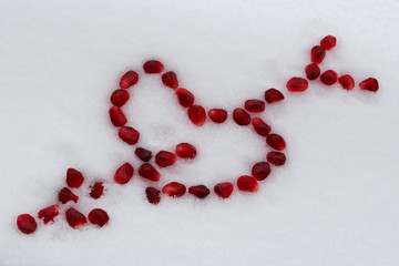 Valentine's heart shape with arrow made by pomegranate seeds on white snow. Valentine's Day concept. Selective focus.