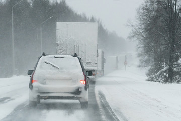 The car is driving on a winter road in a blizzard