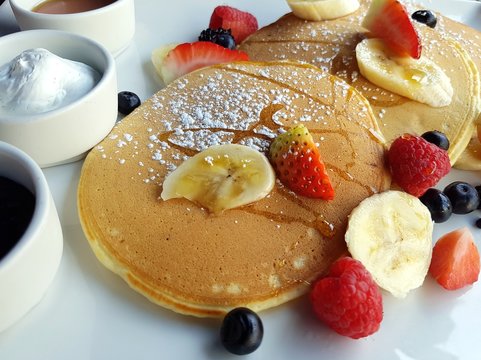 Close-up picture of a sweet breakfast composed of pancakes, fresh berries and fruits, ricotta cheese, jam and honey. Delicious start of a day.