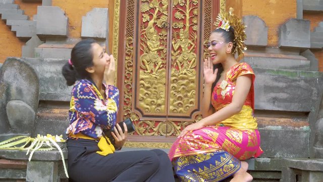 Balinese woman wearing traditional clothes and talking with a reporter or photographer while sitting in the temple. Shot in 4k resolution