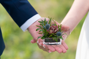 glass box decorated with flowers with wedding rings in the hands of the newlyweds