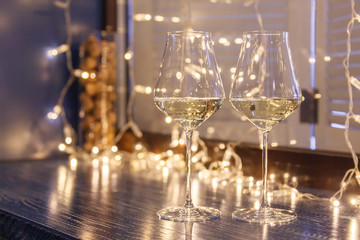 Closeup of two glasses of white wine in transparent crystal glasses on background of window and garlands. Concept romantic dinner in Michelin premium restaurant, party, February 14, March 8