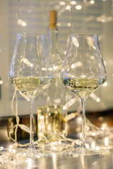 Closeup of two glasses of white wine in transparent crystal glasses on background of window and garlands. Concept romantic dinner in Michelin premium restaurant, party, February 14, March 8