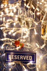 Closeup strawberry, two crystal glasses, bottle champagne sparkling wine, reserved nameplate wooden table, window, garlands. Concept date evening restaraunt, 8 march, Valentine's Day, christmas
