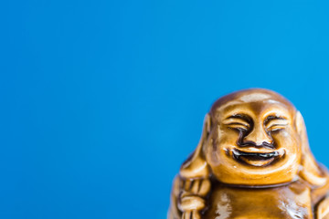 Fototapeta na wymiar Generic statue of laughing Buddha on sky blue background. Buddhism religious symbol. Zen tranquility harmony concept. Minimalist inspirational image with copy space for quotes.