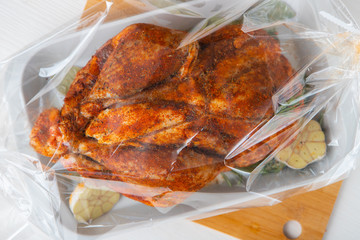 Raw guinea fowl smeared with spices with paprika lies on a white dish for baking with garlic and rosemary - all this lies in a transparent bag for baking