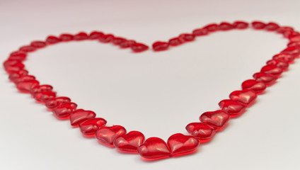 Heart-shaped laid out of small glass red hearts on white background. Valentine's Day. Symbol of love. Copy space.