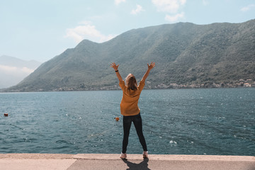 Obraz premium life style. travel and freedom. Hands up. Girl on the background of the mountains of Montenegro is standing, jumping in the old town by the sea