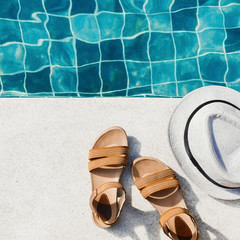 Vacation flat lay with woman's sandals and hat front of the pool