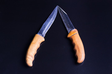 two knives with wooden handles lay a blade to the blade, on a black background
