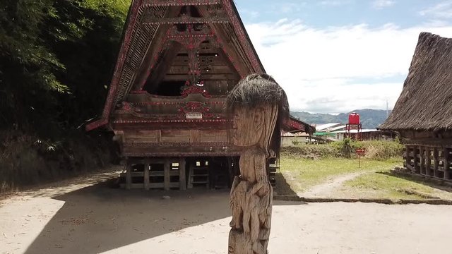 Drone rising with a totem pole in the foreground at traditional Batak houses on Samosir Island in lake Toba, Sumatra, Indonesia.