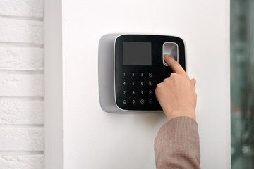 Woman scanning fingerprint on alarm system indoors, closeup